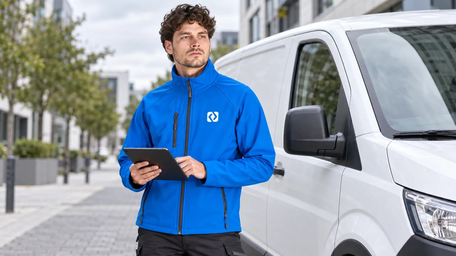 Service technician in a blue softshell jacket with a chest logo next to a van